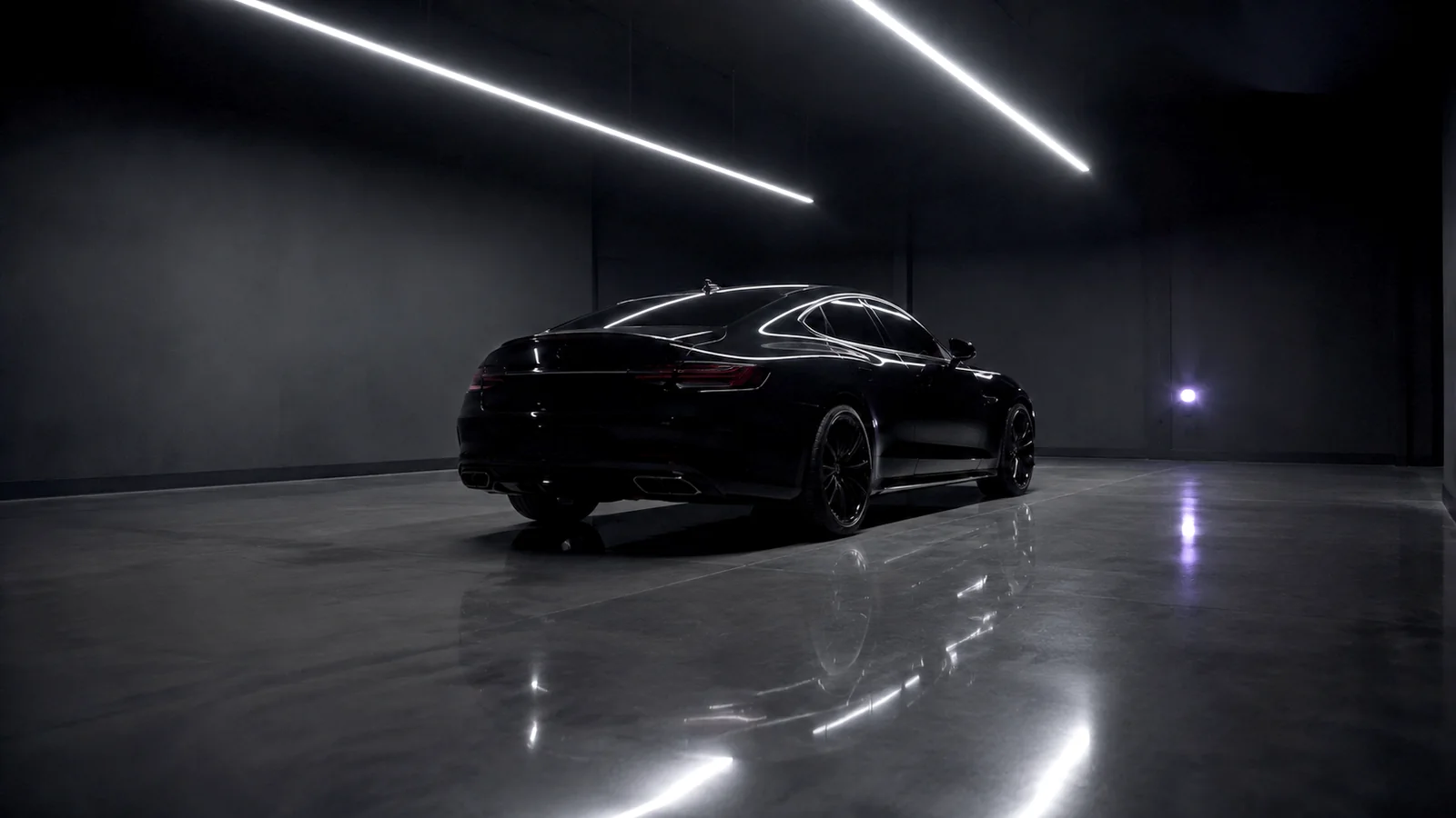 Interior del taller de noche: un auto negro bajo dos tiras de LED, con el piso de concreto pulido reflejando las luces.